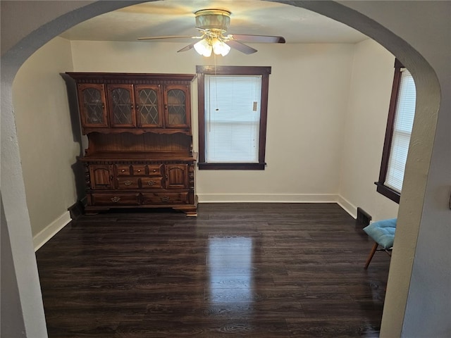 empty room featuring ceiling fan, dark wood-type flooring, and a healthy amount of sunlight