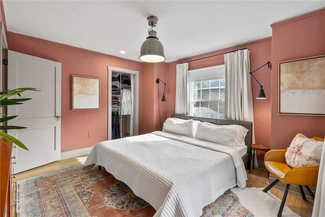 bedroom with crown molding, a spacious closet, a closet, and light wood-type flooring