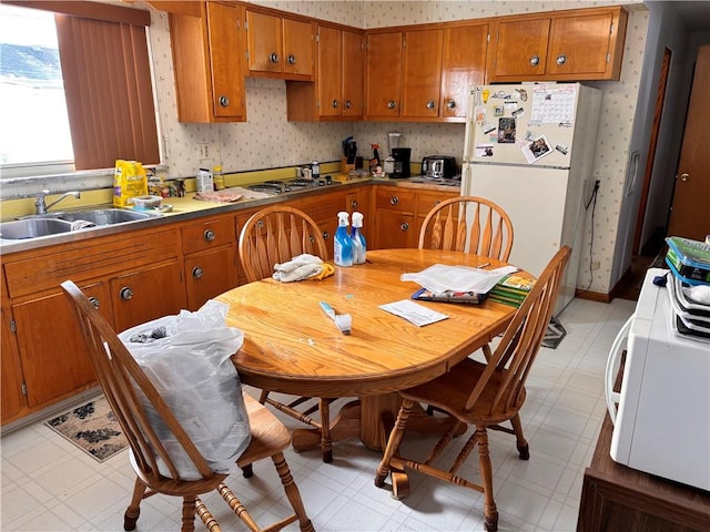 kitchen with brown cabinets, a sink, light floors, and wallpapered walls