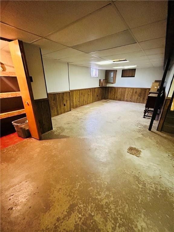 basement with a drop ceiling and wood walls