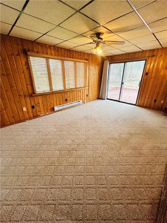 unfurnished room featuring wood walls, a drop ceiling, and a baseboard heating unit