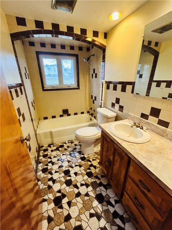 full bathroom featuring tile walls, vanity, toilet, and tiled shower / bath