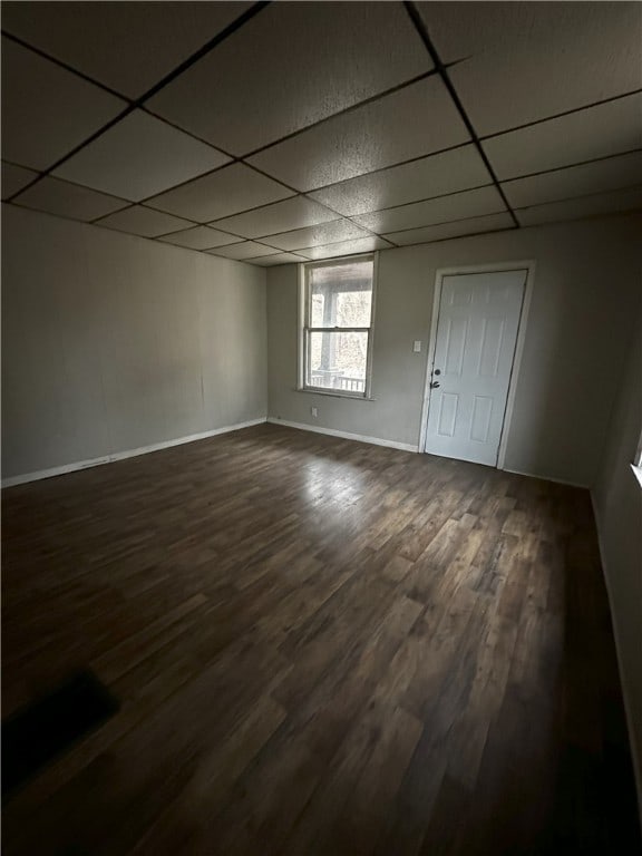 empty room featuring baseboards, a paneled ceiling, and dark wood-type flooring