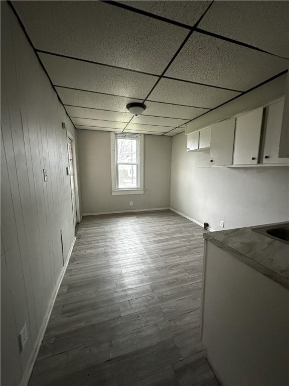 interior space with a drop ceiling, baseboards, and wood finished floors