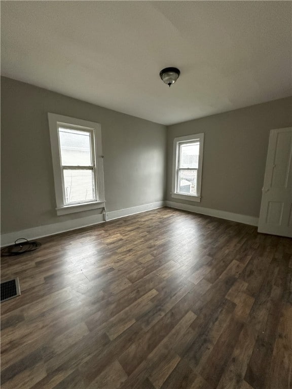 empty room with visible vents, baseboards, and dark wood-style flooring