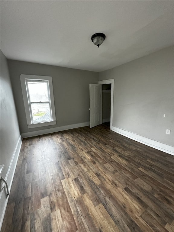 unfurnished room with baseboards and dark wood-type flooring