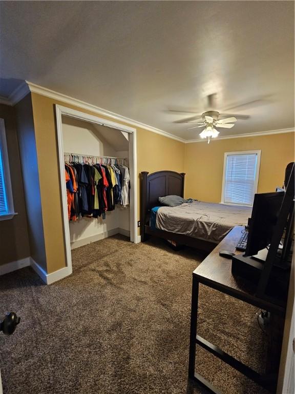 bedroom with ornamental molding, ceiling fan, dark carpet, and a closet