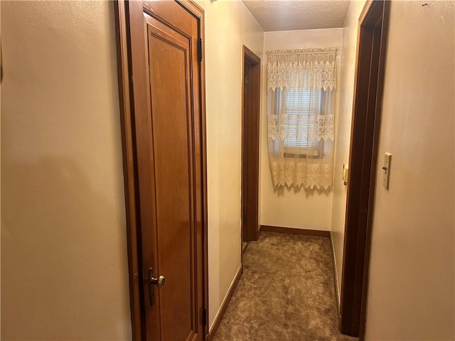 hall with a textured ceiling and dark colored carpet