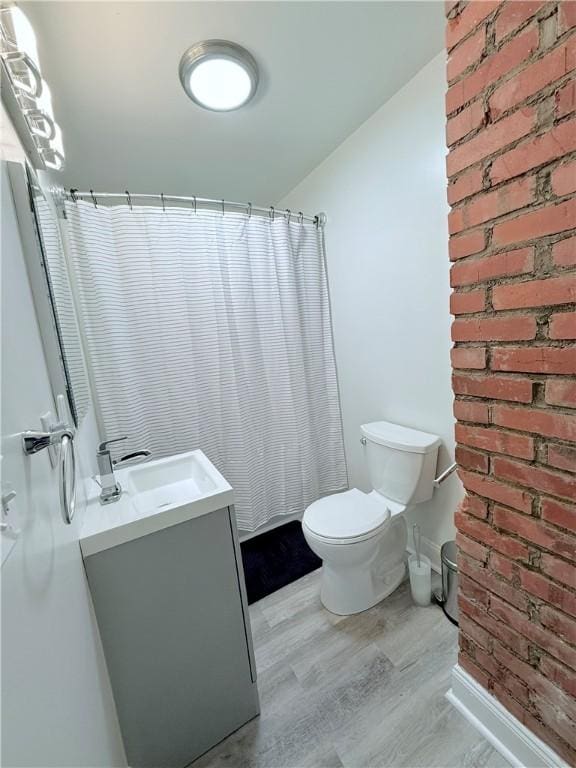 bathroom with vanity, wood-type flooring, brick wall, curtained shower, and toilet