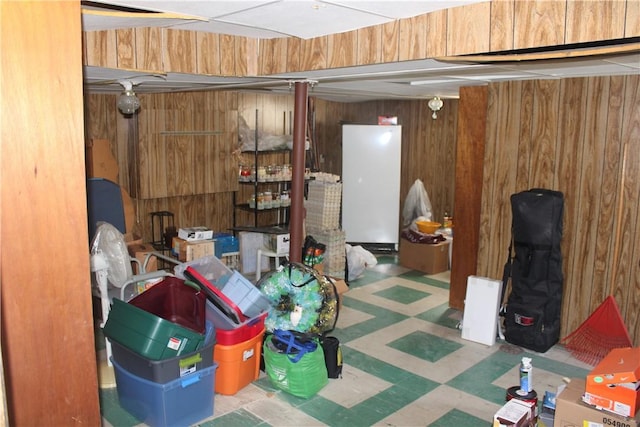 basement with white refrigerator and wooden walls