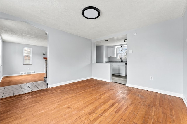 unfurnished living room featuring a tiled fireplace, sink, light hardwood / wood-style floors, and a textured ceiling