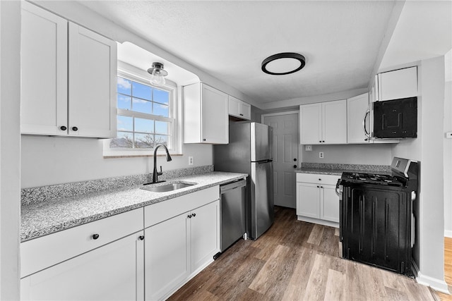 kitchen with appliances with stainless steel finishes, sink, white cabinets, and light wood-type flooring