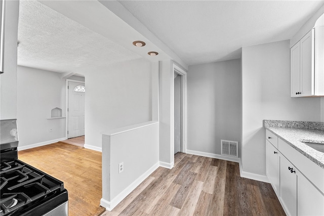 kitchen featuring sink, light hardwood / wood-style flooring, gas range oven, a textured ceiling, and white cabinets