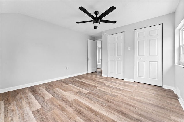 unfurnished bedroom featuring ceiling fan, light hardwood / wood-style flooring, and multiple closets