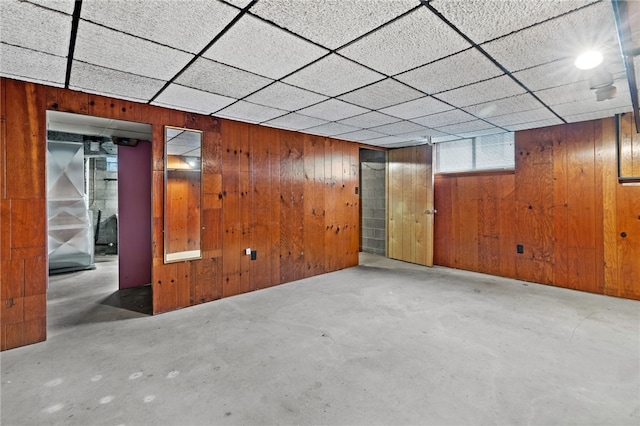 unfurnished room with a drop ceiling and wood walls