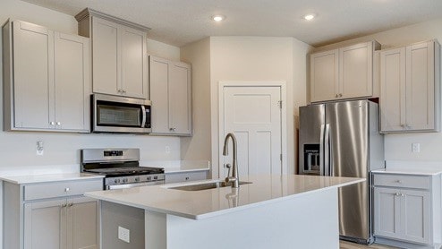 kitchen featuring sink, gray cabinets, an island with sink, and appliances with stainless steel finishes