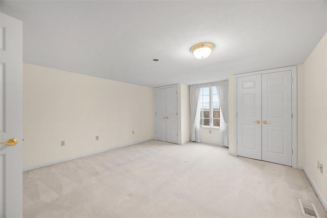 unfurnished bedroom with light carpet and two closets