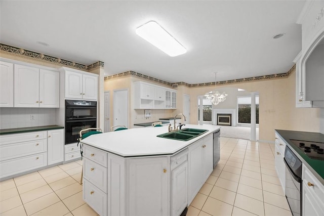 kitchen with pendant lighting, double oven, white cabinetry, an island with sink, and sink