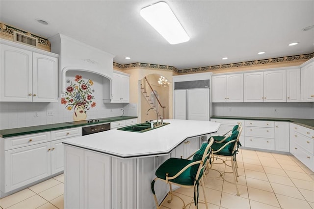 kitchen featuring tasteful backsplash, white cabinetry, sink, light tile patterned floors, and a center island with sink