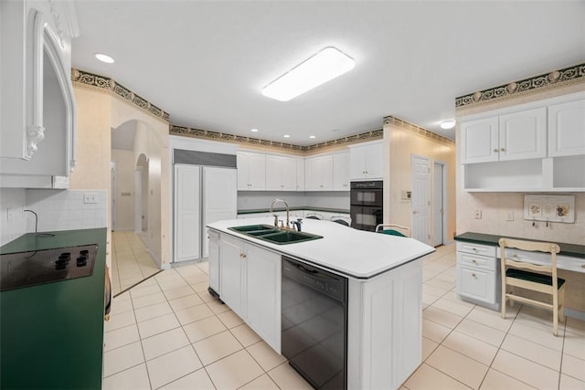 kitchen featuring sink, white cabinetry, light tile patterned floors, a kitchen island with sink, and black appliances