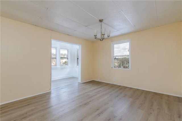 empty room featuring an inviting chandelier, wood finished floors, and baseboards