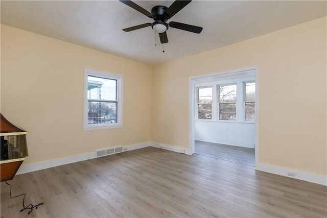 empty room with visible vents, baseboards, wood finished floors, and a healthy amount of sunlight