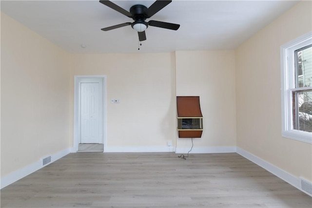 empty room with visible vents, a ceiling fan, light wood finished floors, and baseboards