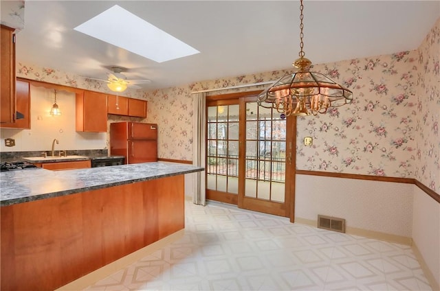 kitchen featuring hanging light fixtures, sink, ceiling fan, fridge, and a skylight