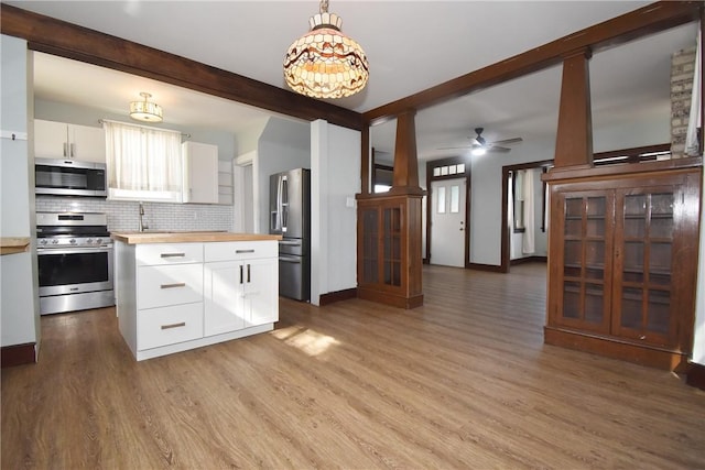 kitchen featuring stainless steel appliances, wood counters, pendant lighting, beamed ceiling, and white cabinetry