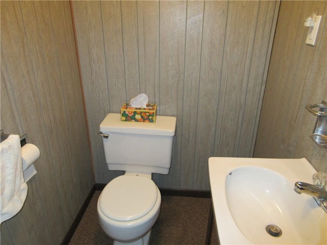 bathroom with sink, wood walls, and toilet