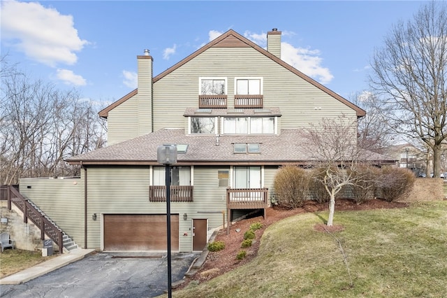 rear view of property with a balcony, a garage, and a lawn