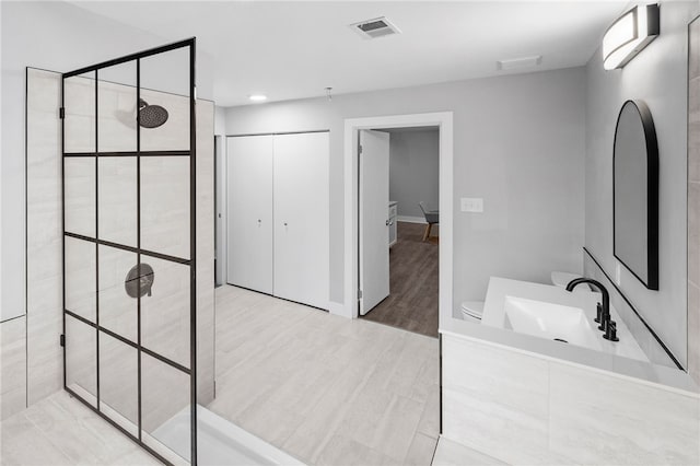 bathroom with hardwood / wood-style flooring, vanity, tiled shower, and toilet