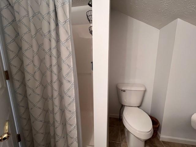 bathroom featuring tile patterned floors, a shower with curtain, toilet, and a textured ceiling