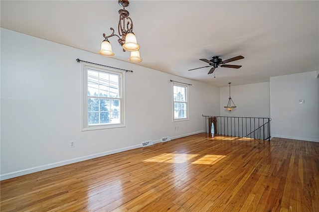 spare room with ceiling fan with notable chandelier and light wood-type flooring