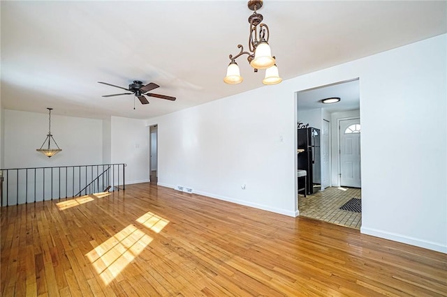 spare room with ceiling fan with notable chandelier and light hardwood / wood-style flooring