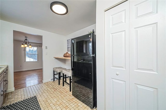 kitchen featuring a chandelier, pendant lighting, tile patterned flooring, and black fridge