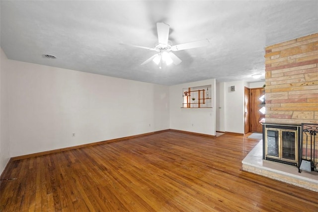 unfurnished living room featuring ceiling fan, wood-type flooring, a stone fireplace, and a textured ceiling