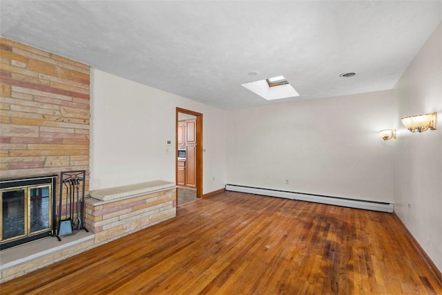 unfurnished living room featuring baseboard heating, wood-type flooring, a skylight, and a fireplace