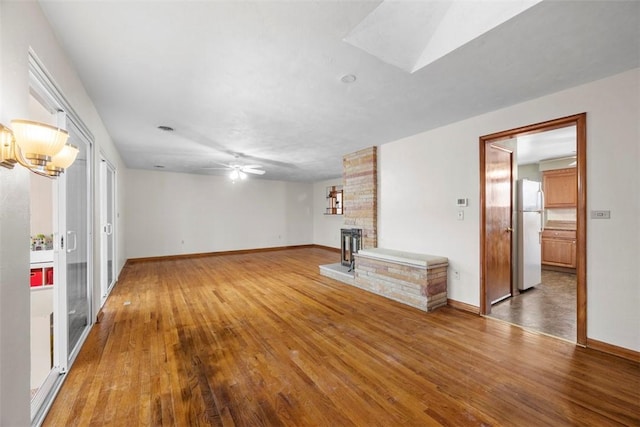 unfurnished living room featuring a fireplace, a skylight, hardwood / wood-style floors, and ceiling fan