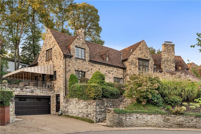 view of front of home featuring a garage, stone siding, a chimney, and driveway