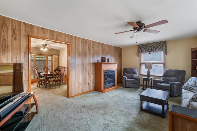 living room with a glass covered fireplace, carpet flooring, ceiling fan, and wooden walls