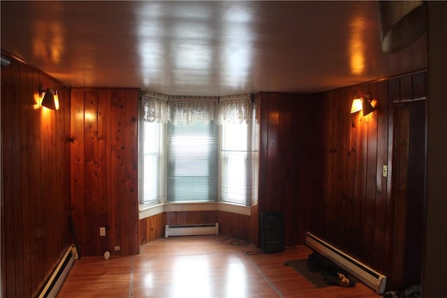 unfurnished room with wood-type flooring, a baseboard radiator, and wooden walls