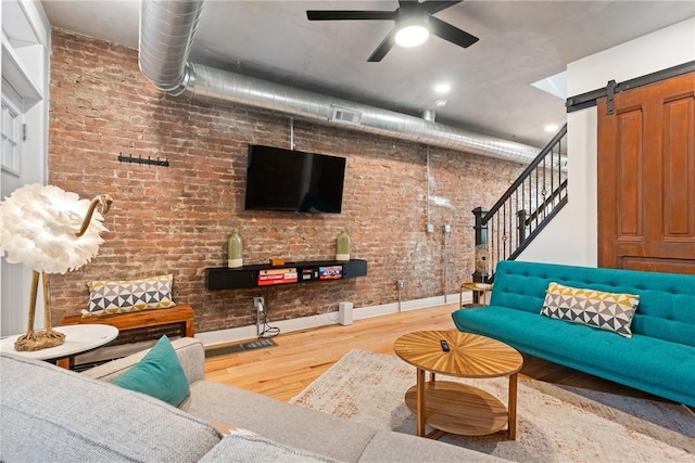 living room featuring brick wall, ceiling fan, wood-type flooring, and a barn door