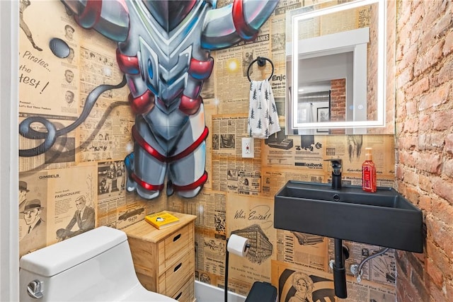 interior space with brick wall, sink, and toilet