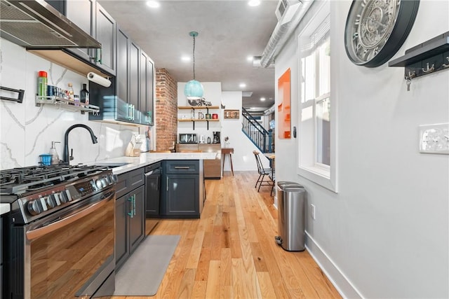 kitchen with pendant lighting, light hardwood / wood-style floors, wall chimney exhaust hood, stainless steel gas range, and tasteful backsplash