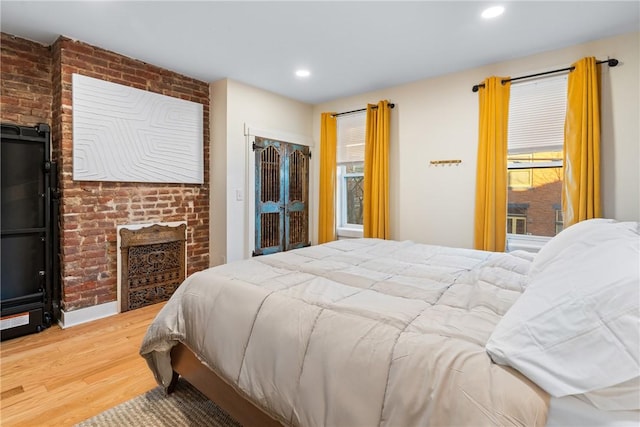 bedroom with hardwood / wood-style floors, brick wall, and a fireplace