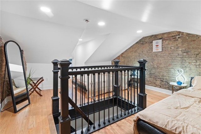 bedroom featuring vaulted ceiling, brick wall, and wood-type flooring