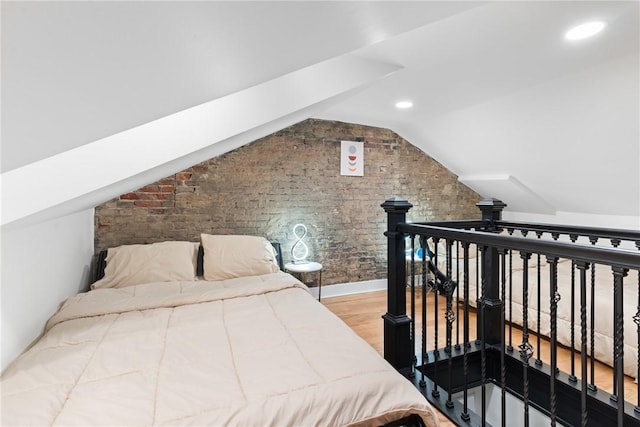 bedroom featuring brick wall, hardwood / wood-style flooring, and lofted ceiling