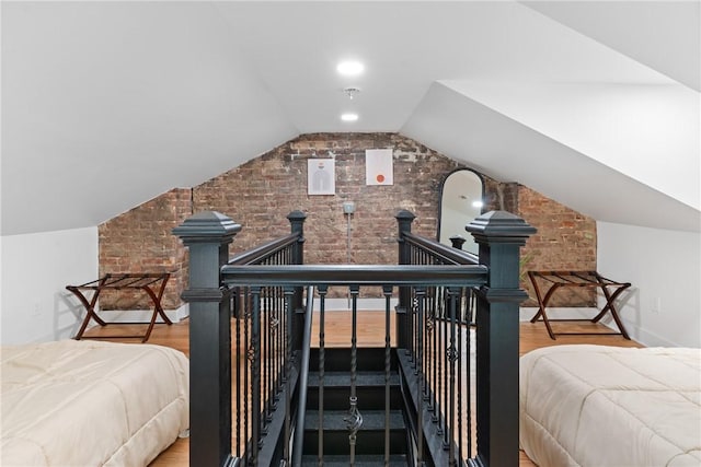 bedroom featuring brick wall, vaulted ceiling, and hardwood / wood-style floors