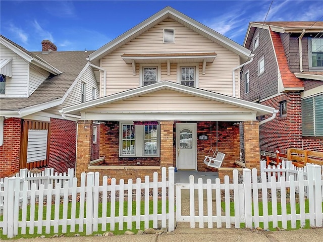 view of front facade with a fenced front yard, brick siding, and roof with shingles